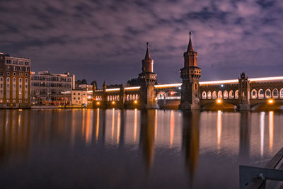 Illuminated oberbaum bridge over spree river against cloudy sky