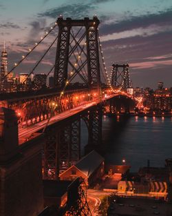 Illuminated bridge over river in city against sky at night