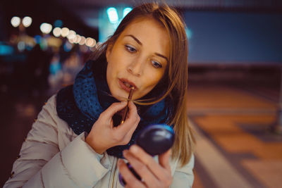 Beautiful woman applying lipstick at night