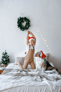 A boy and a dog in red santa hat having fun on bed. best friends. christmas mood. festive atmosphere