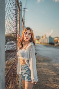 Portrait of beautiful young woman standing against sky