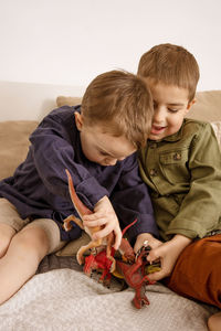 Two little and cute caucasian boys playing with dinosaurs at home.