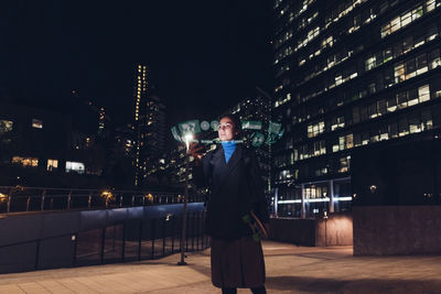 Woman using augmented reality standing on footpath at night