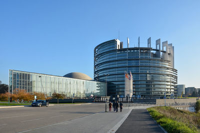 People walking on modern building against clear blue sky