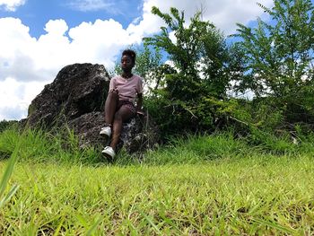 Low angle view of woman sitting on field against sky