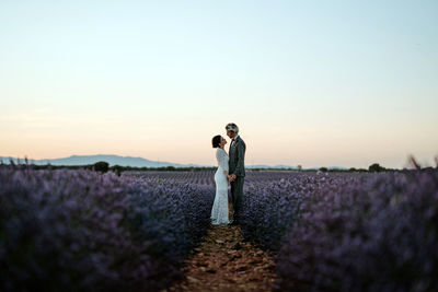 Couple standing on field against sky during sunset