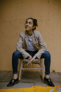 Portrait of smiling young woman sitting against wall