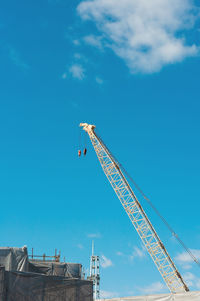 Low angle view of crane by building against blue sky