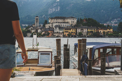 Rear view of man standing by lake against boat and orta san giulio island