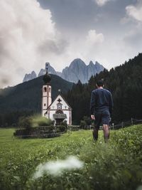 Rear view of man walking on land leading towards church against sky