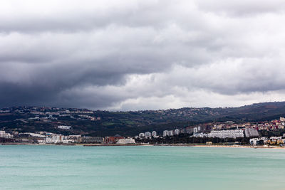 Buildings by sea against cloudy sky