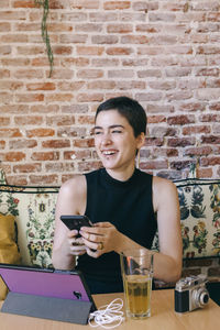 Smiling young woman using laptop on table against brick wall