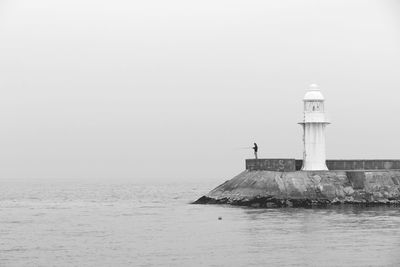 Lighthouse by sea against clear sky