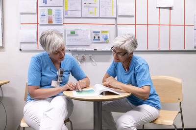Female doctors discussing medical records while sitting on chairs in hospital