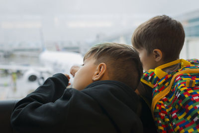 Brothers looking through window while waiting at airport departure area