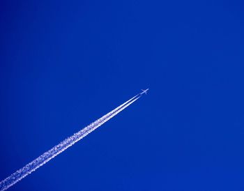 Low angle view of airplane flying against clear blue sky