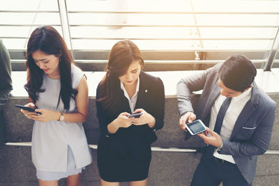 Colleagues using phones while standing at elevated walkway 