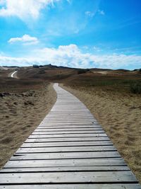 Boardwalk amidst field against blue sky