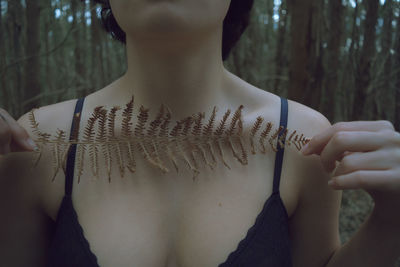 Midsection of woman wearing bra while holding leaf outdoors