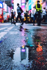 Reflection of people walking on illuminated street in puddle at night