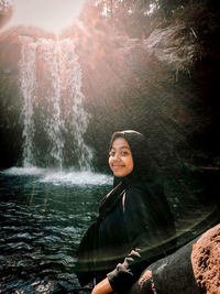 Portrait of smiling young woman against waterfall