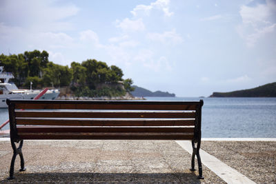 Empty bench by sea against sky