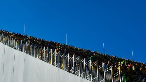 Low angle view of crowd at stadium against clear blue sky on sunny day