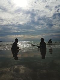 Silhouette men on beach against sky during sunset
