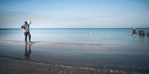 Boy standing on beach against sky