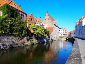 View of buildings against blue sky, reflected in canal water, in bruges