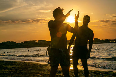 Rear view of man standing at beach during sunset