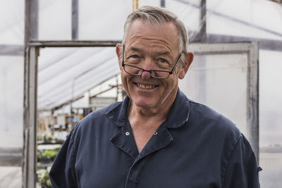 Portrait of smiling man wearing eyeglasses while standing against greenhouse