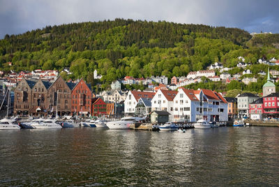 Sailboats in river by houses against buildings in city