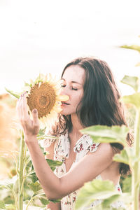 Young woman holding flowering plant against white wall