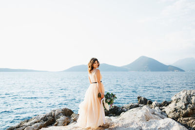 Woman standing on rock by sea against sky