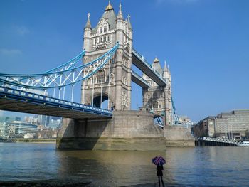 Rear view of woman carrying umbrella standing against tower bridge