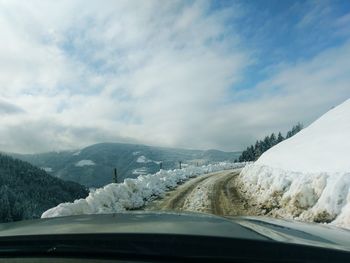 Road amidst snowcapped mountains seen through car windshield