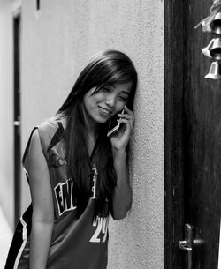 Young woman talking on phone by wall