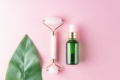 Pink jade stone facial roller, serum lotion, moisturizer, on pink background. flat lay, top view.