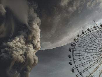 Low angle view of ferris wheel against smoke came from eruption of taal volcano