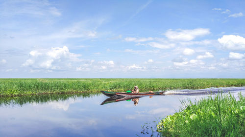Man on boat sailing in river amidst grassy landscape