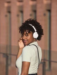 Attractive l teenage girl with curly hair listening to music with white headphones on the street. 