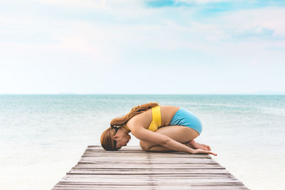 Side view of woman doing yoga on pier at beach