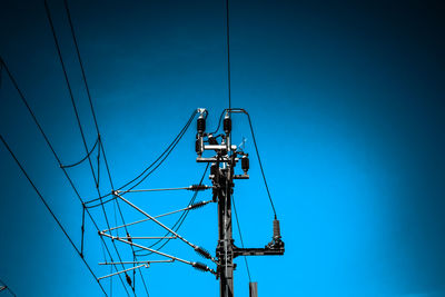 Low angle view of electricity pylon against clear blue sky