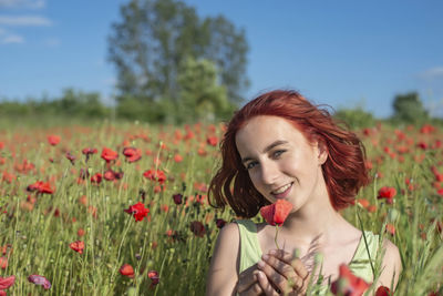 Portrait of young woman blowing flowers on field