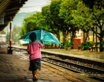Rear view of boy with umbrella walking on railroad station