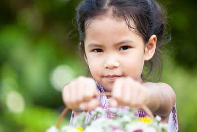 Portrait of cute girl holding basket with flowers while standing in yard