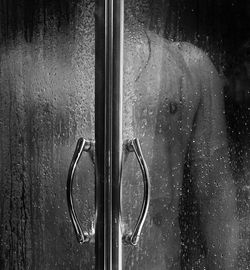 Midsection of shirtless man seen through wet glass door