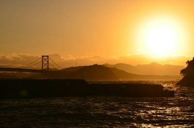 Silhouette bridge over sea against orange sky