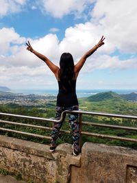 Rear view of woman with arms raised against sky